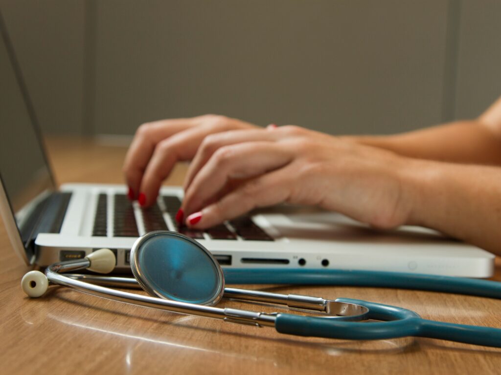 Woman's hands type on laptop with stethoscope lying on the table